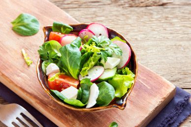 A bowl of salad on top of a wooden board.