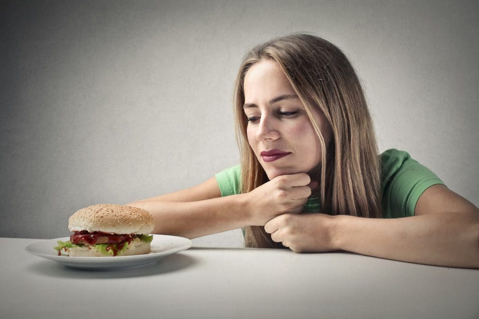 A woman sitting at the table with a sandwich in front of her.