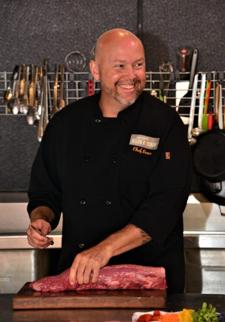 A man in black jacket holding meat on top of a cutting board.